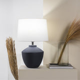 Buriti Table Lamp by Geo Contemporary in Navy Blue with a White shade on a console beside dried grasses