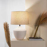 Buriti Table Lamp by Geo Contemporary in White with a Rustic Linen shade on a console beside dried grasses