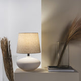 Cedro Table Lamp by Geo Contemporary with a Rustic Linen shade on a console beside dried grasses