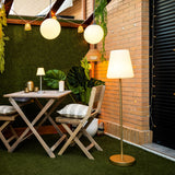 Lola Slim Solar Floor Lamp - Brass, lit in a courtyard garden