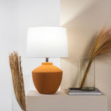 Buriti Table Lamp by Geo Contemporary in Terracotta with a White shade on a console beside dried grasses