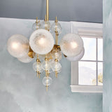 Calypso 6 Light Chandelier by Hudson Valley in Aged Brass hanging by a window