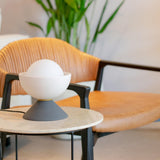 Don Ceramic Table Lamp by Geo Contemporary in White and Graphite, lit, on a marble side table beside a leather chair