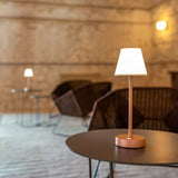 Lola Slim Portable Table Lamp - Rose Gold, lit on a cafe table