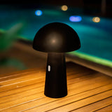 Shitake Portable Table Lamp - Black, lit on a poolside deck