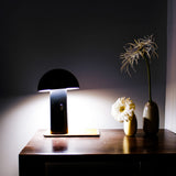Shitake Portable Table Lamp - Black, lit on a sideboard