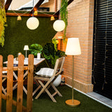 Lola Slim Solar Floor Lamp - Brass, in a courtyard garden